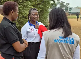 A young woman peacebuilder speaks with two women wearing UN Women vests